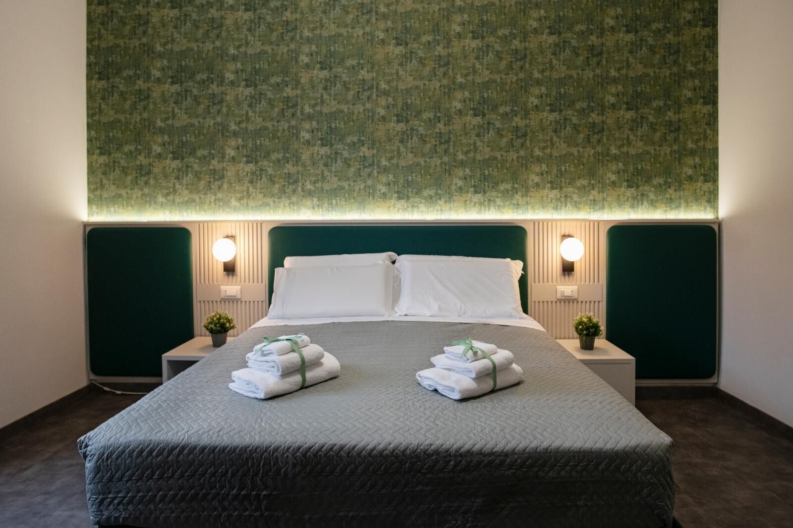 A neatly made bed with a green headboard, two bedside tables with lamps, and a green textured wall.