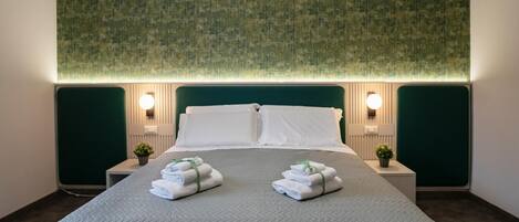 A neatly made bed with a green headboard, two bedside tables with lamps, and a green textured wall.