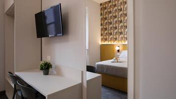 A hotel room with a desk, a TV mounted on the wall, a bed with a headboard, and a patterned wall decoration.