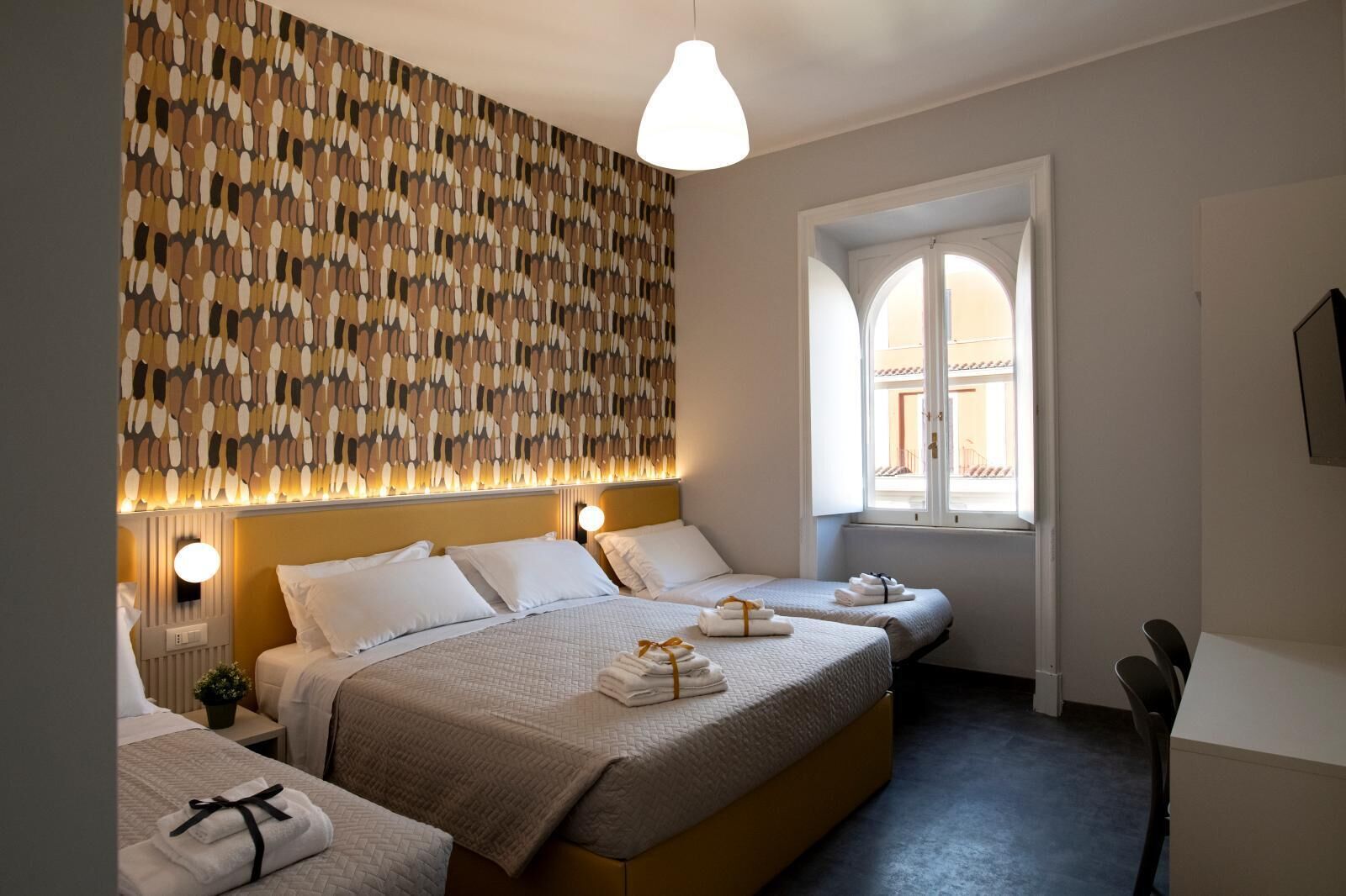 Une chambre d’hôtel avec un grand lit, deux tables de chevet, une lampe fixée au mur, une fenêtre avec vue et un téléviseur mural.