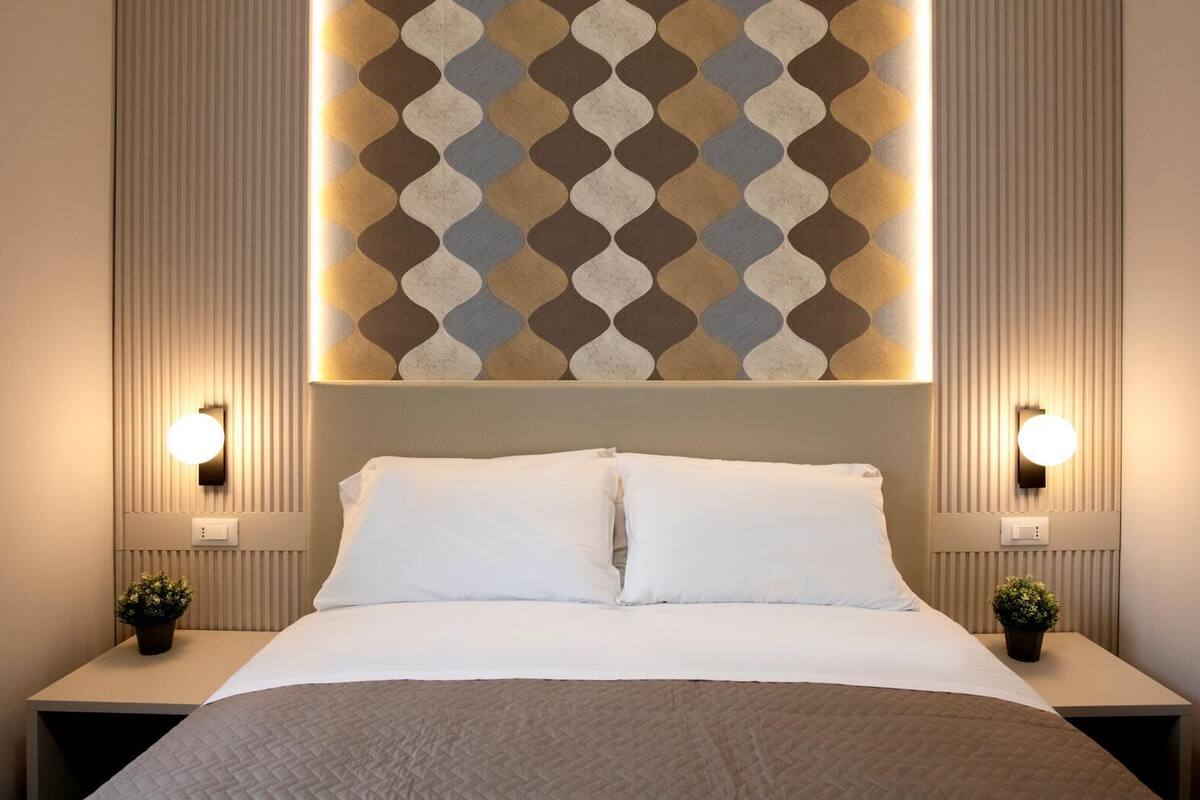 Ein Hotelzimmer mit einem großen Bett, zwei Nachttischen und einer Wandleuchte mit geometrischem Muster.