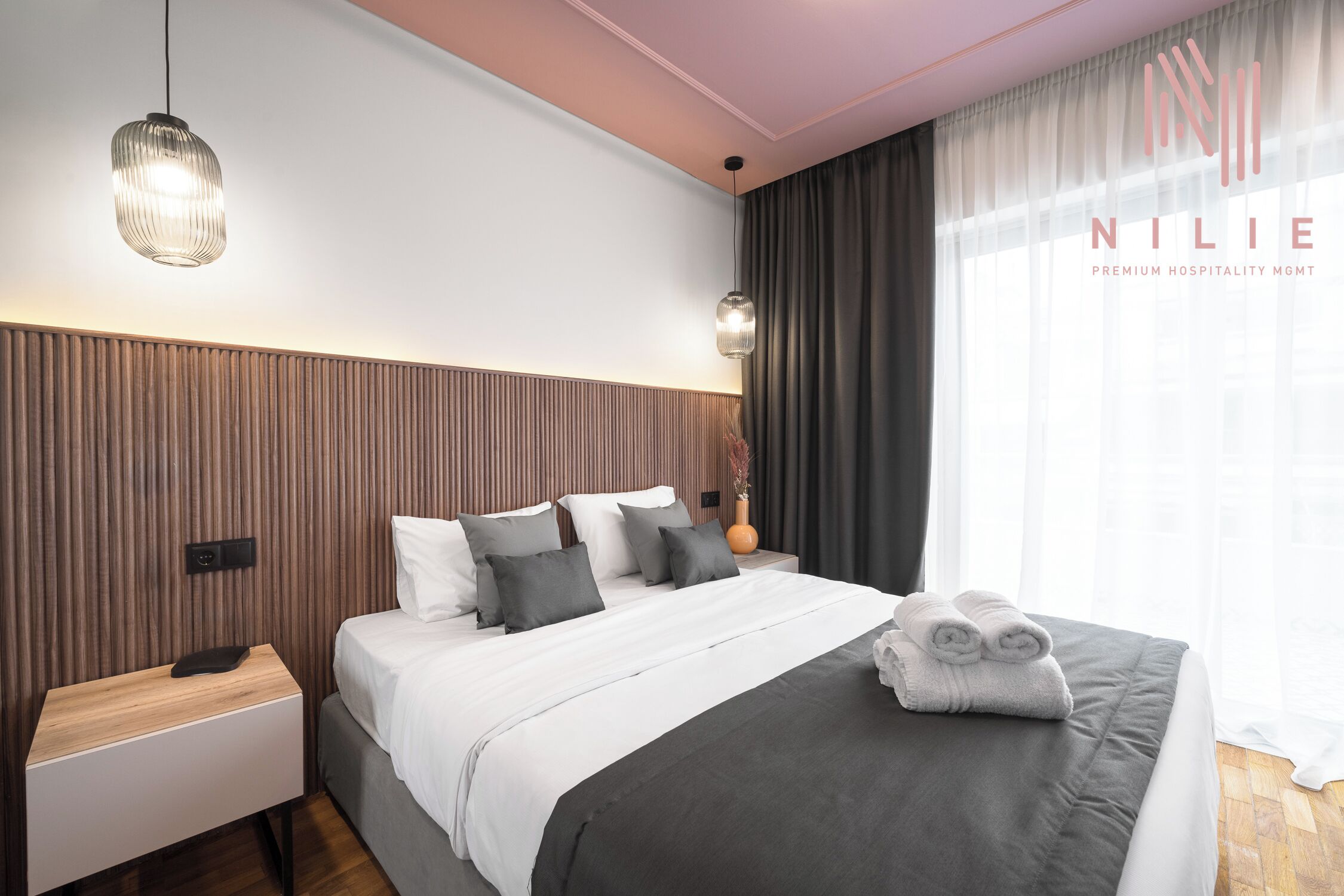 Una habitación de hotel moderna con una cama grande, un cabecero de madera, una mesita de noche y una mesilla.