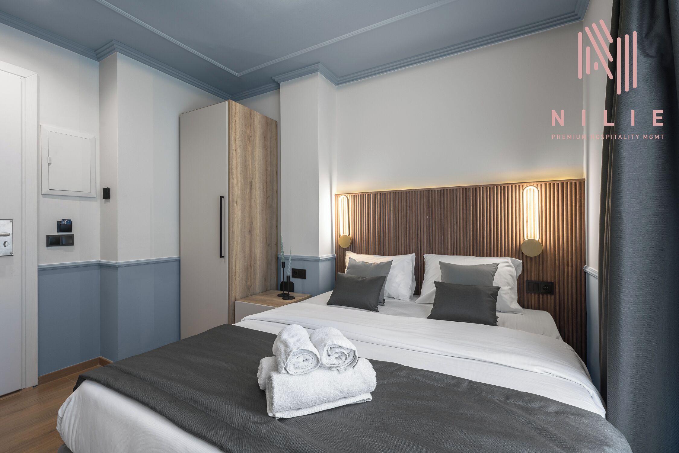 Ein modernes Hotelzimmer mit einem ordentlich bezogenen Bett, einem Holzkopfende und einem Nachttisch mit Lampe.