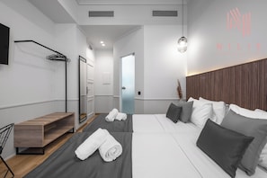 A modern hotel room with a wooden bench, a bed with grey bedding, and a wall-mounted TV. - Esther Suites, Nilie Hospitality MGMT (Thessaloniki)