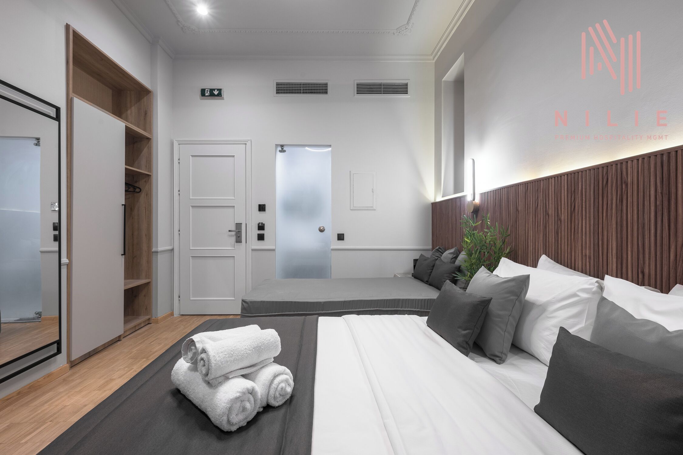 Ein modernes Hotelzimmer mit einem großen Bett, einem Holzschrank, einem Spiegel und Blick auf den Flur.