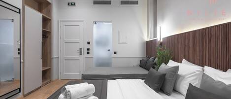A modern hotel room with a large bed, a wooden wardrobe, a mirror, and a view of the hallway.