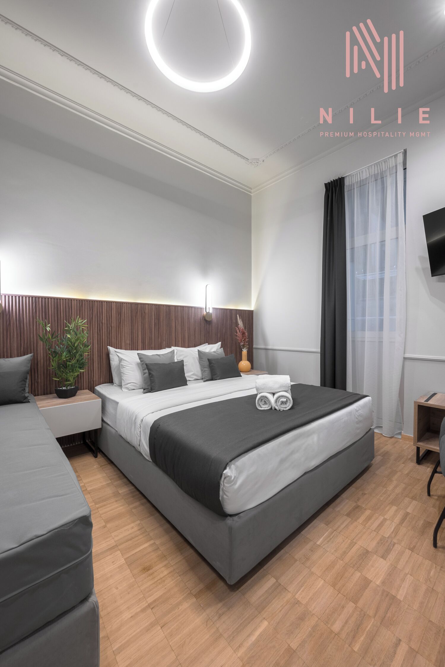 Una habitación de hotel moderna con una cama grande, una mesita de noche, un escritorio pequeño y un televisor montado en la pared.