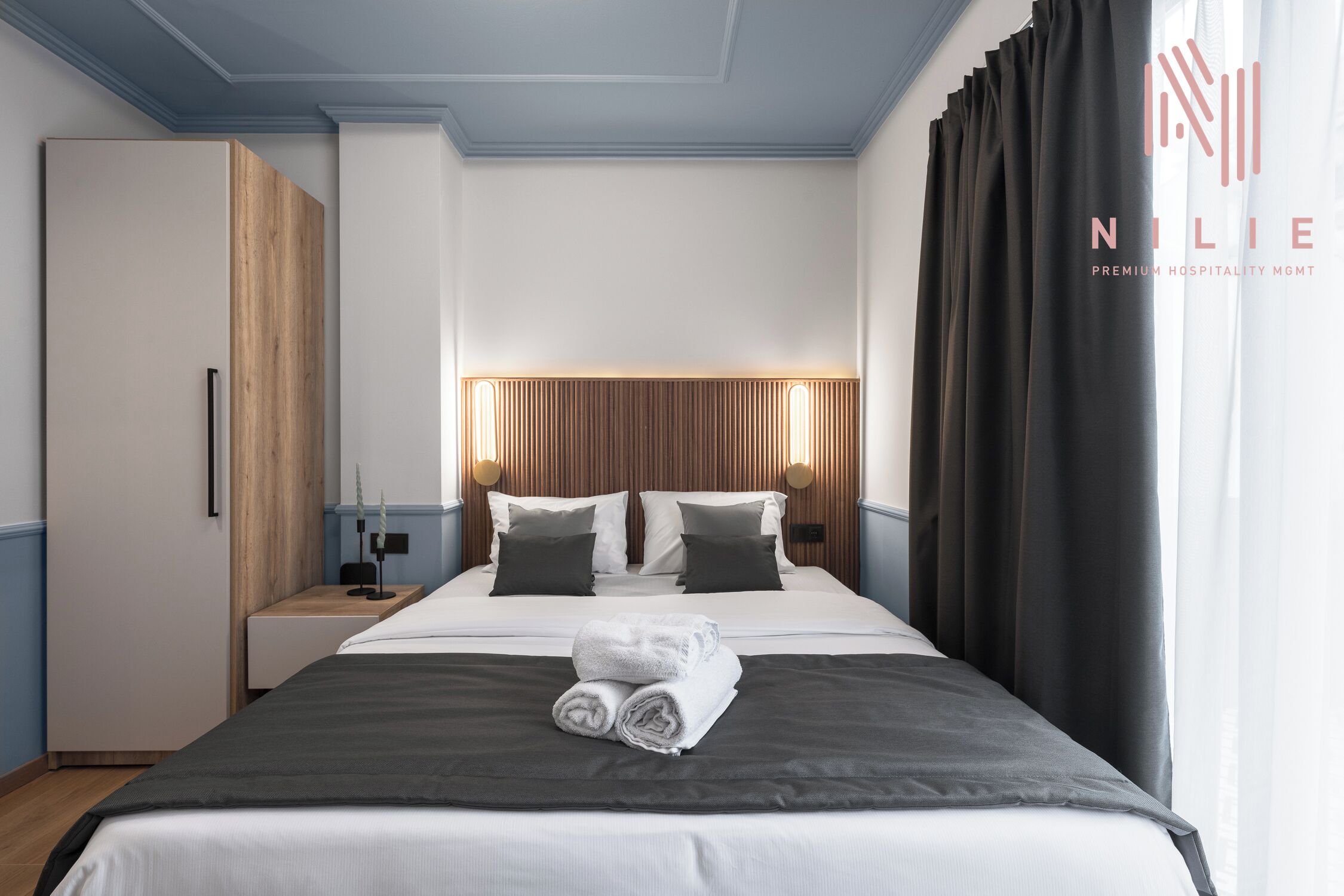 Une chambre d’hôtel avec un grand lit, une tête de lit en bois, deux tables de chevet avec des lampes et une armoire.