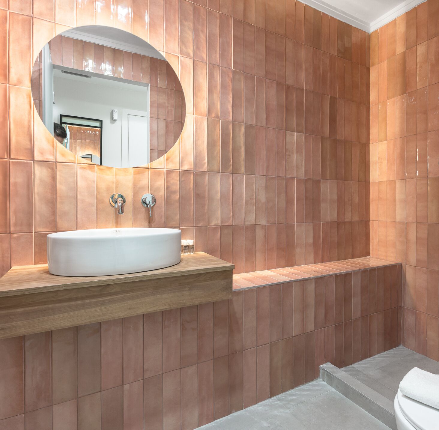 Un baño moderno con un espejo ovalado grande, un lavabo blanco y un mueble de tocador de madera.
