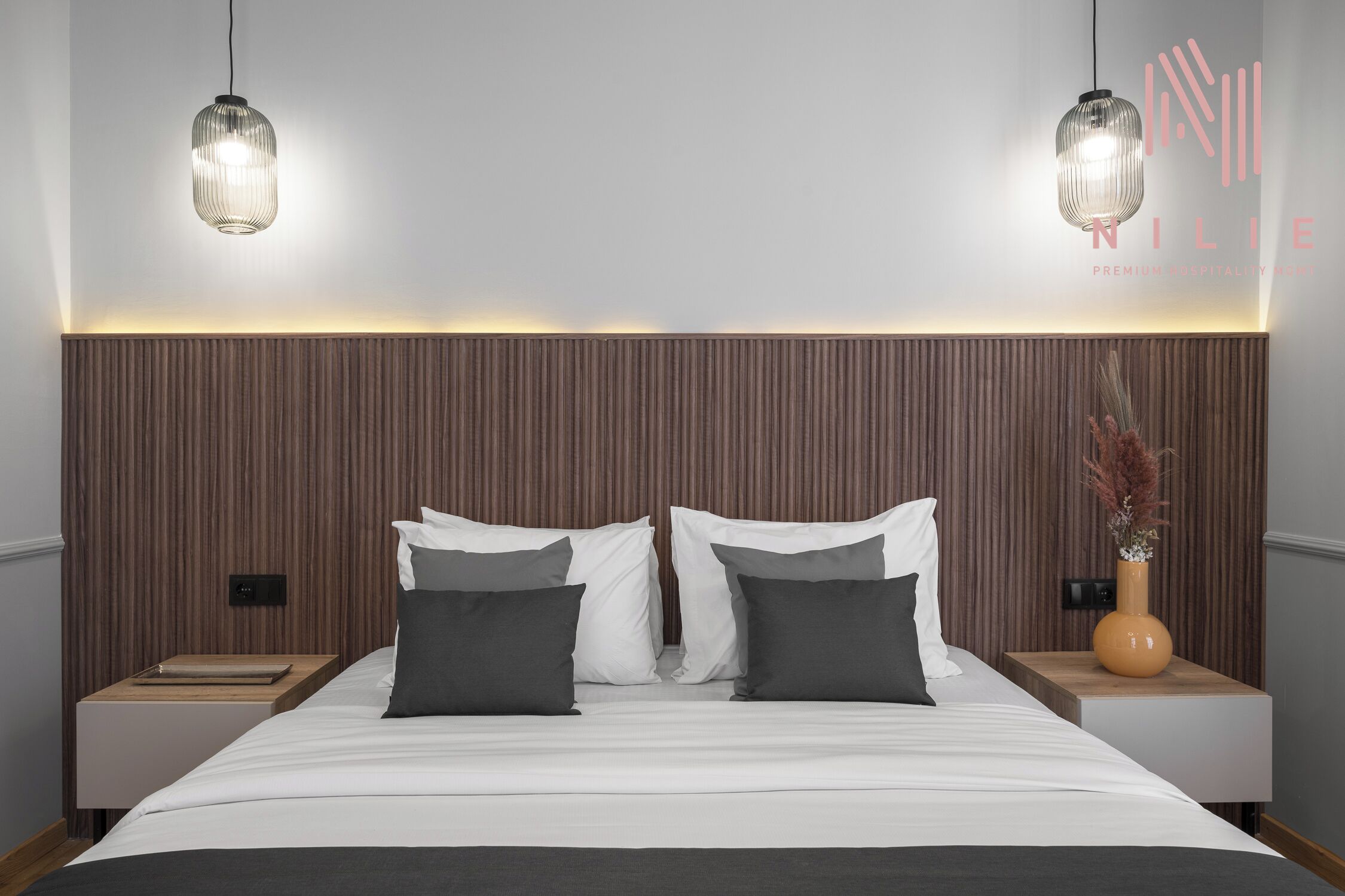 Une chambre d’hôtel moderne avec un grand lit, deux tables de chevet et une tête de lit en bois.