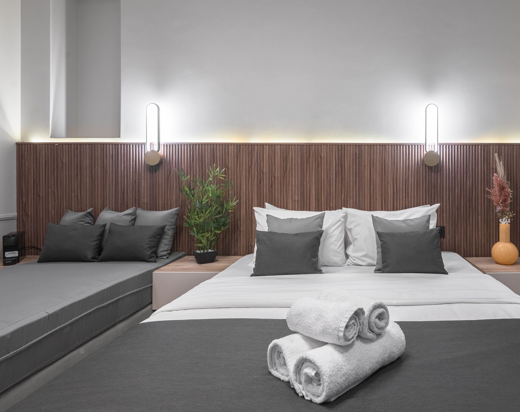 A modern bedroom with a bed, pillows, a bedside table with a plant, and a small table with towels.