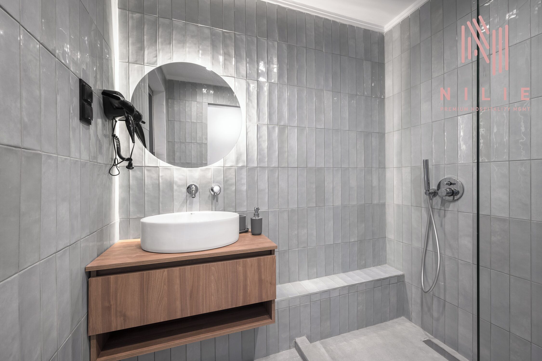 A modern bathroom with a round mirror, a wooden vanity, and a shower area.