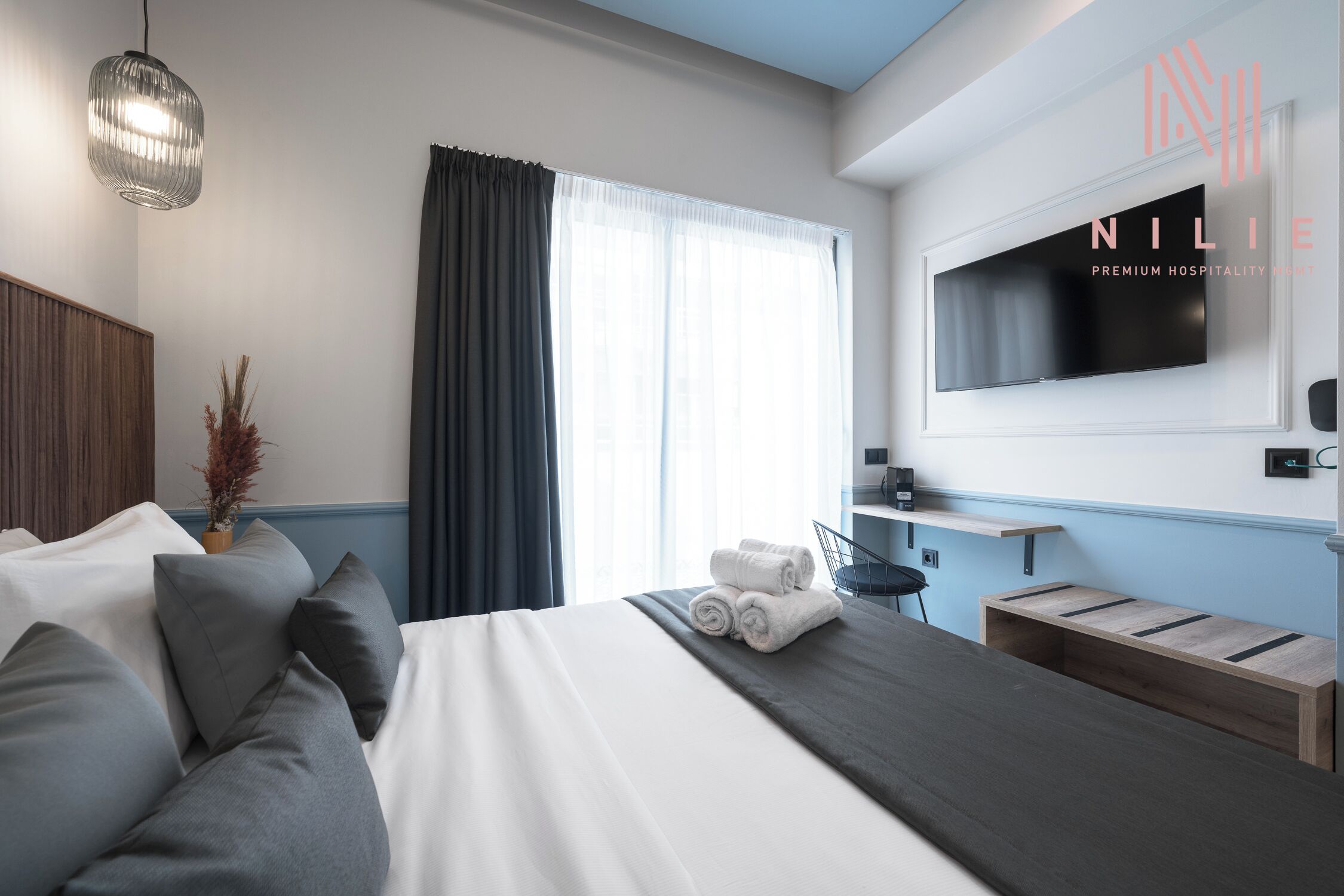 A modern hotel room with a large bed, a TV mounted on the wall, and a window with curtains.