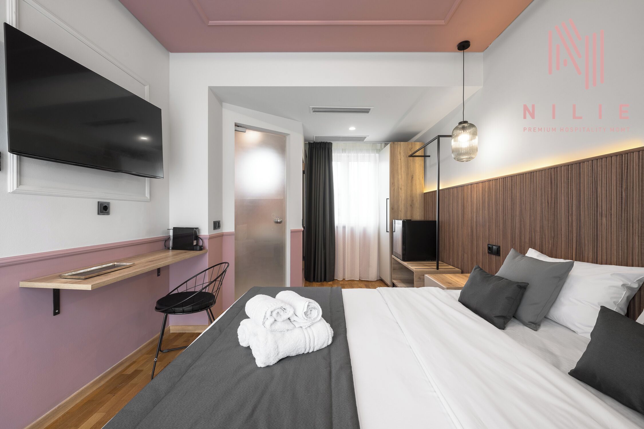 A modern hotel room with a bed, a TV, a bedside table, and a wall-mounted TV.