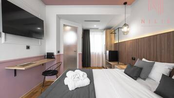 Une chambre d’hôtel moderne équipée d’un lit, d’une télévision, d’une table de chevet et d’un téléviseur fixé au mur.