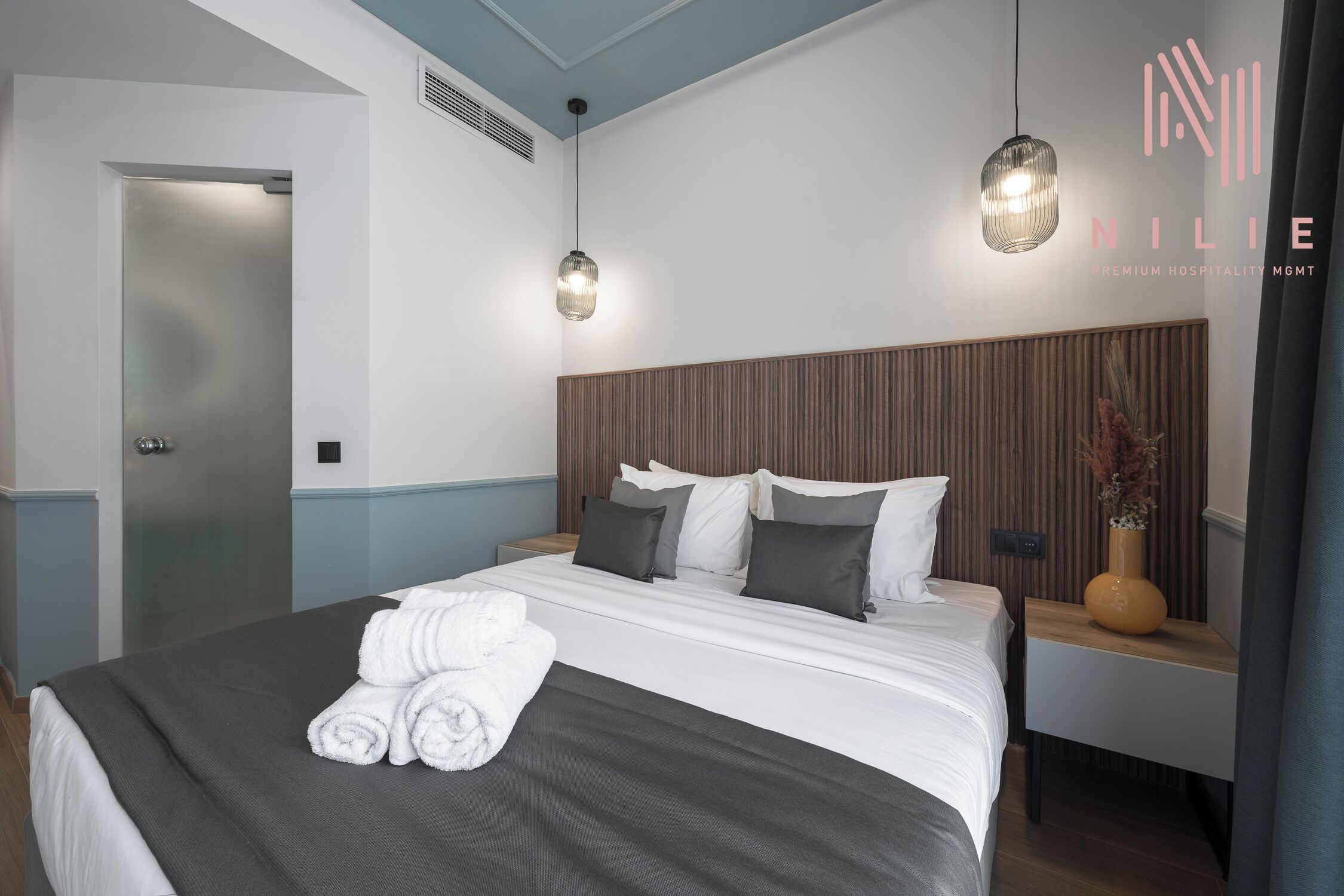 A modern hotel room with a neatly made bed, two bedside tables, and a wall-mounted light fixture.