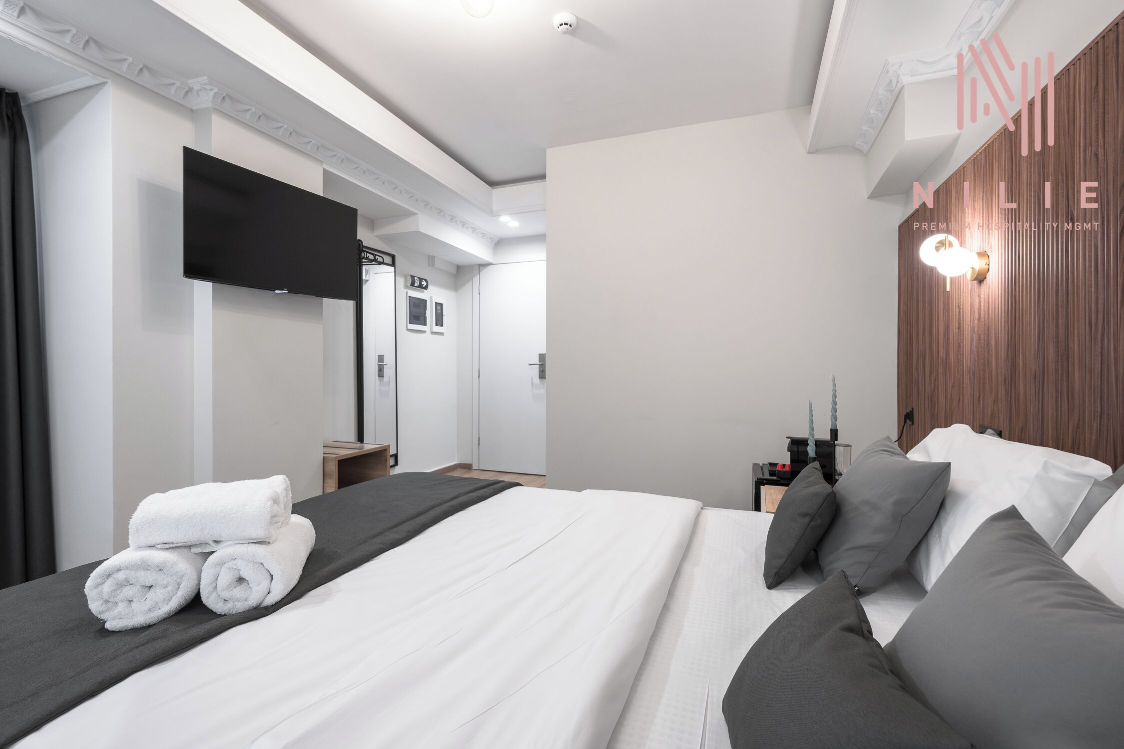 A modern hotel room with a large bed, a flat-screen TV, and a wooden accent wall.