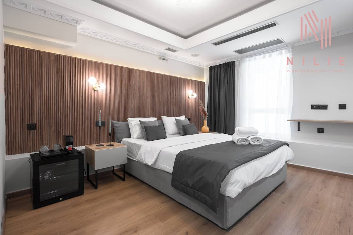 A modern hotel room with a large bed, a bedside table, a coffee maker, and a wall-mounted TV.