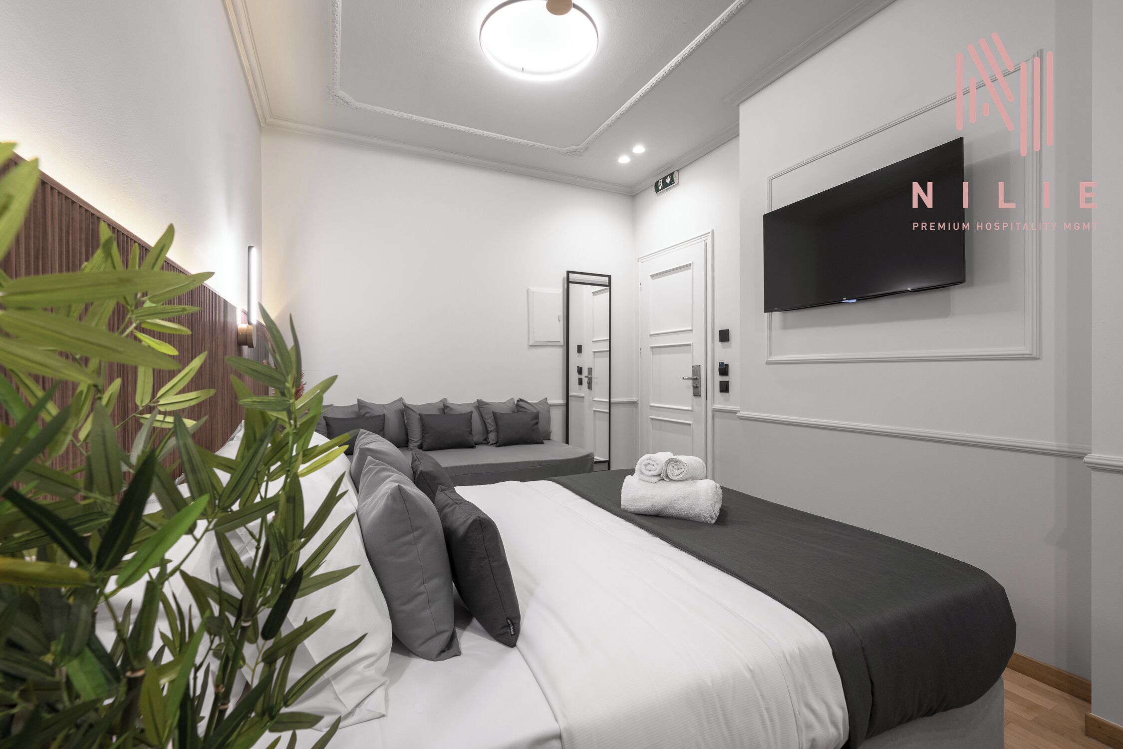 A modern hotel room with a large bed, a flat-screen TV mounted on the wall, and a small seating area.