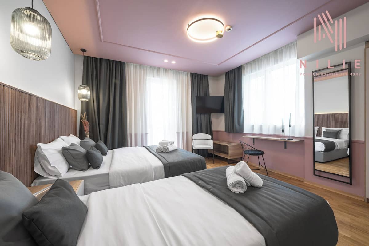 A hotel room with two beds, a desk, a chair, a TV, and a large mirror.
