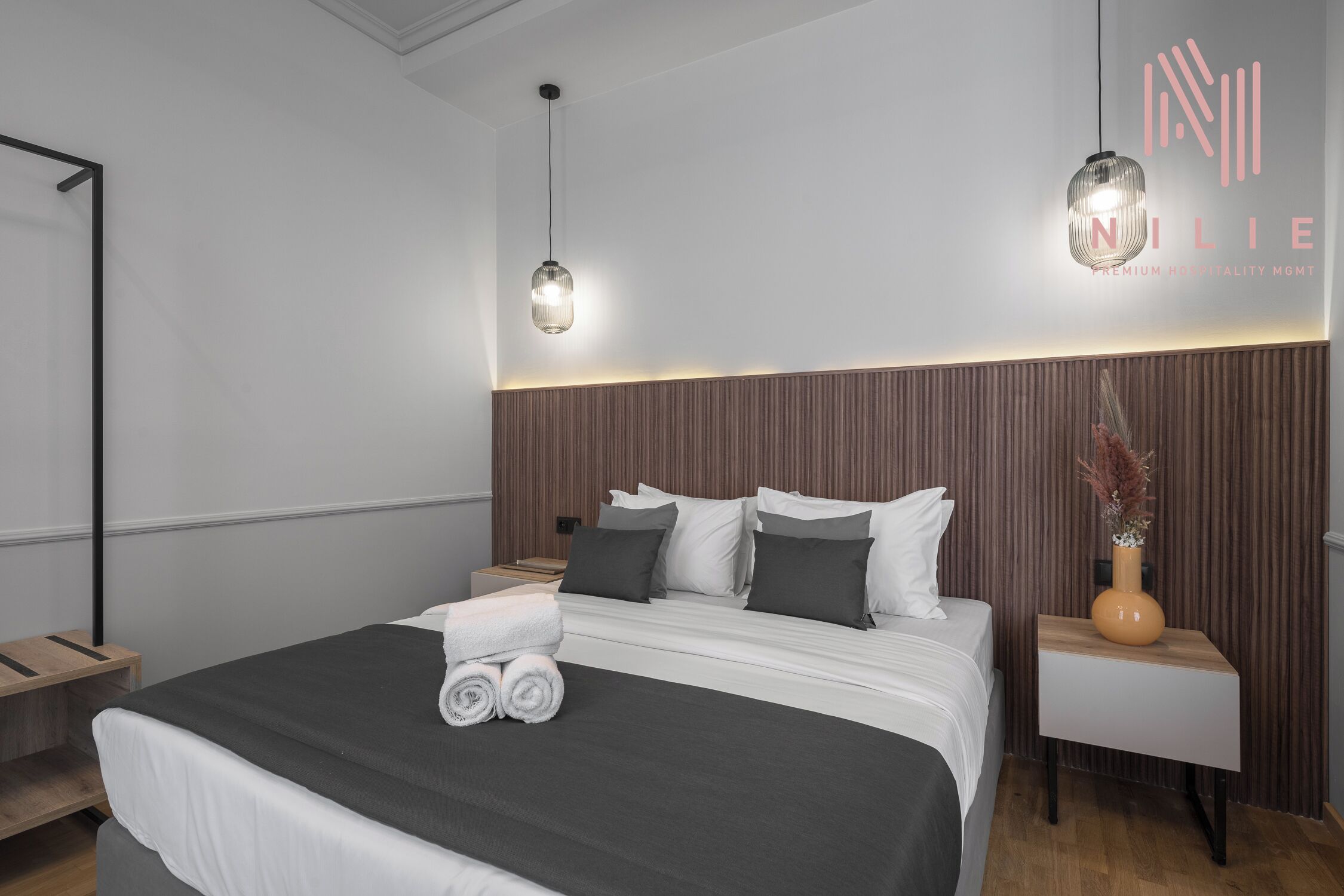 A modern hotel room with a large bed, two bedside tables, and a nightstand.