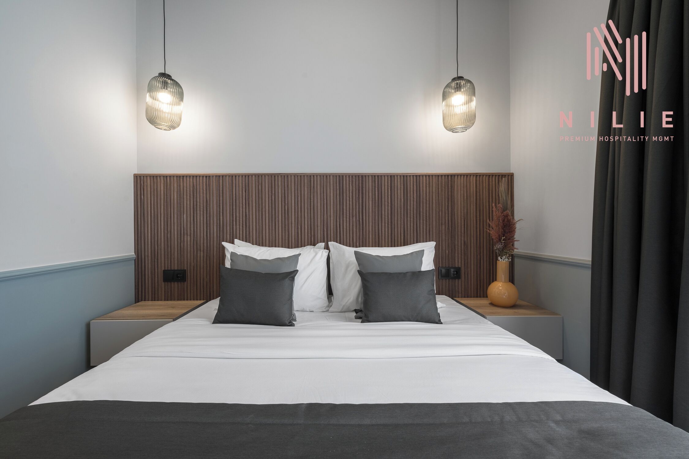 A modern hotel room with a large bed, two bedside tables, and a wooden headboard.