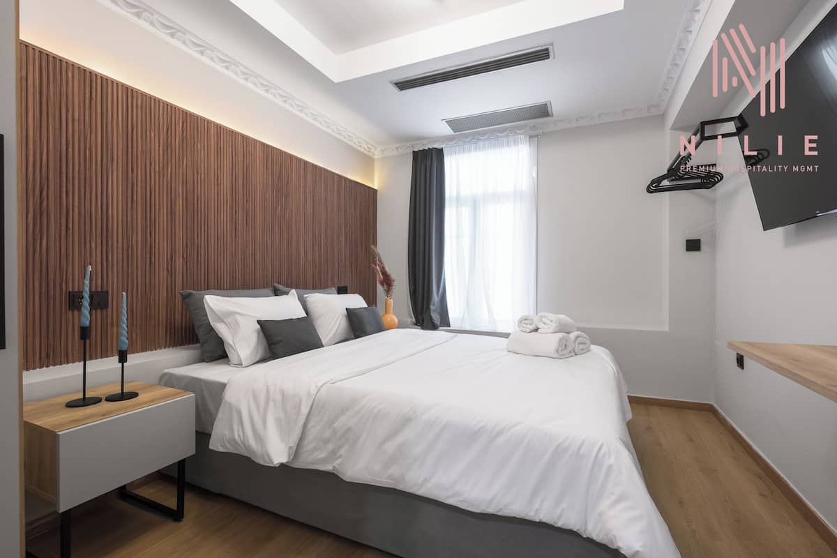 A modern hotel room with a large bed, a bedside table, a TV, and a wooden accent wall.