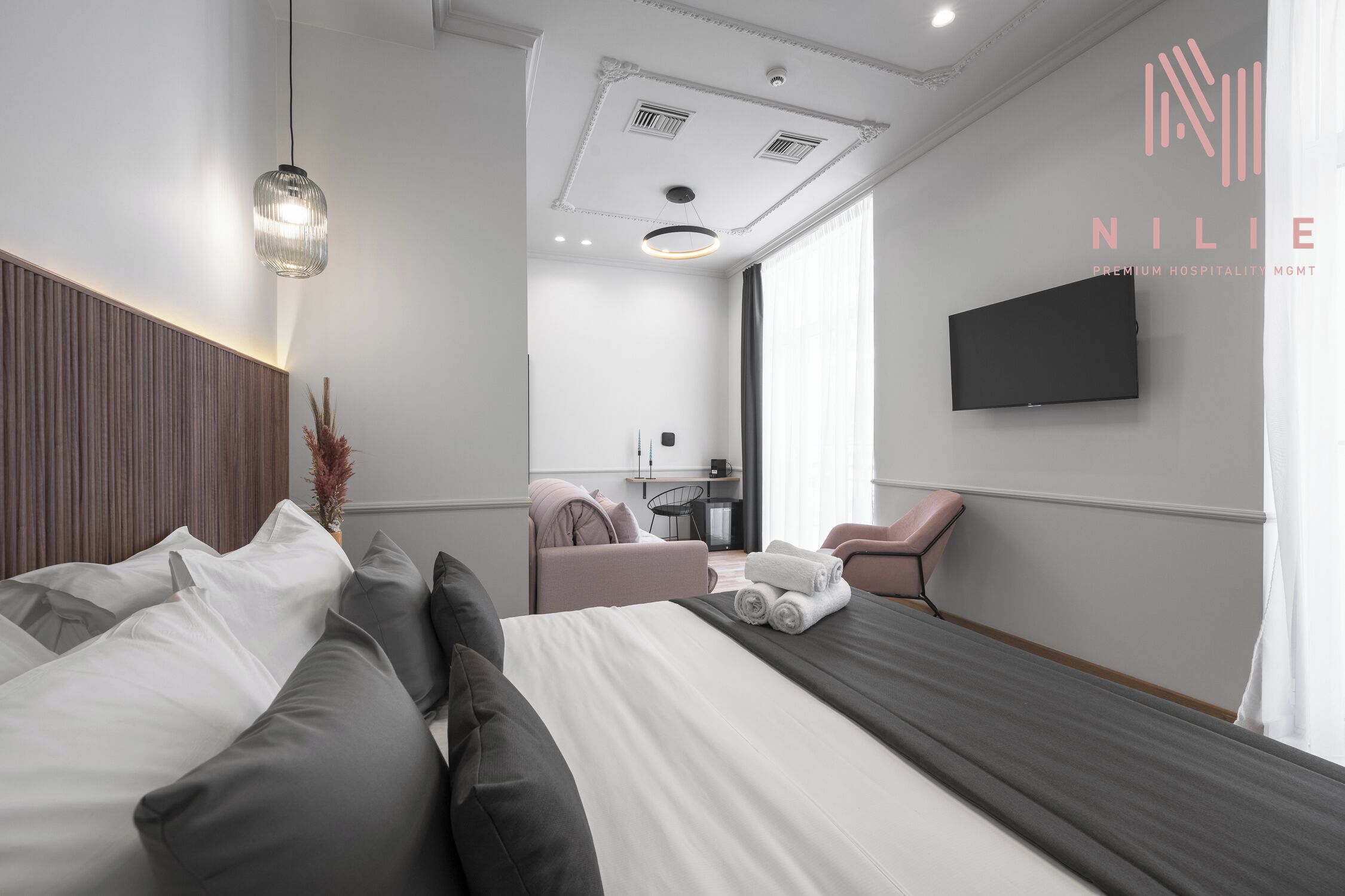 Een moderne hotelkamer met een groot bed, een aan de muur bevestigde televisie en een zithoek met een stoel en een klein tafeltje.