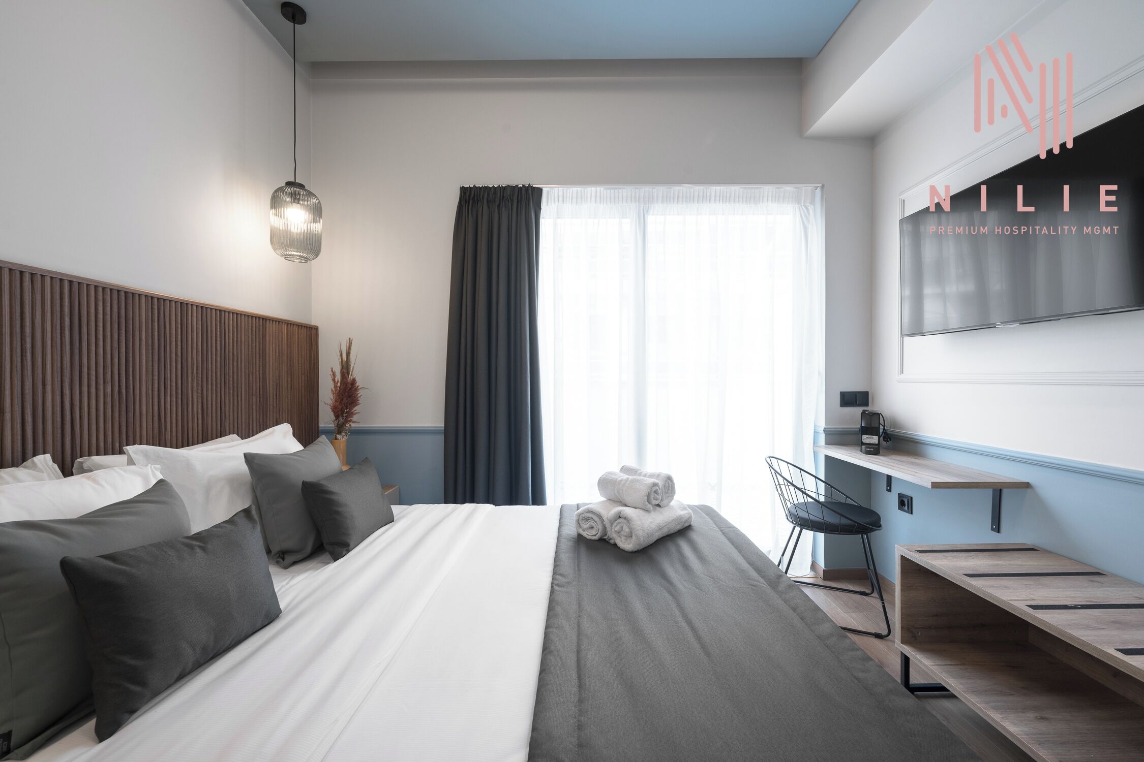 A modern hotel room with a large bed, a desk, and a TV mounted on the wall.