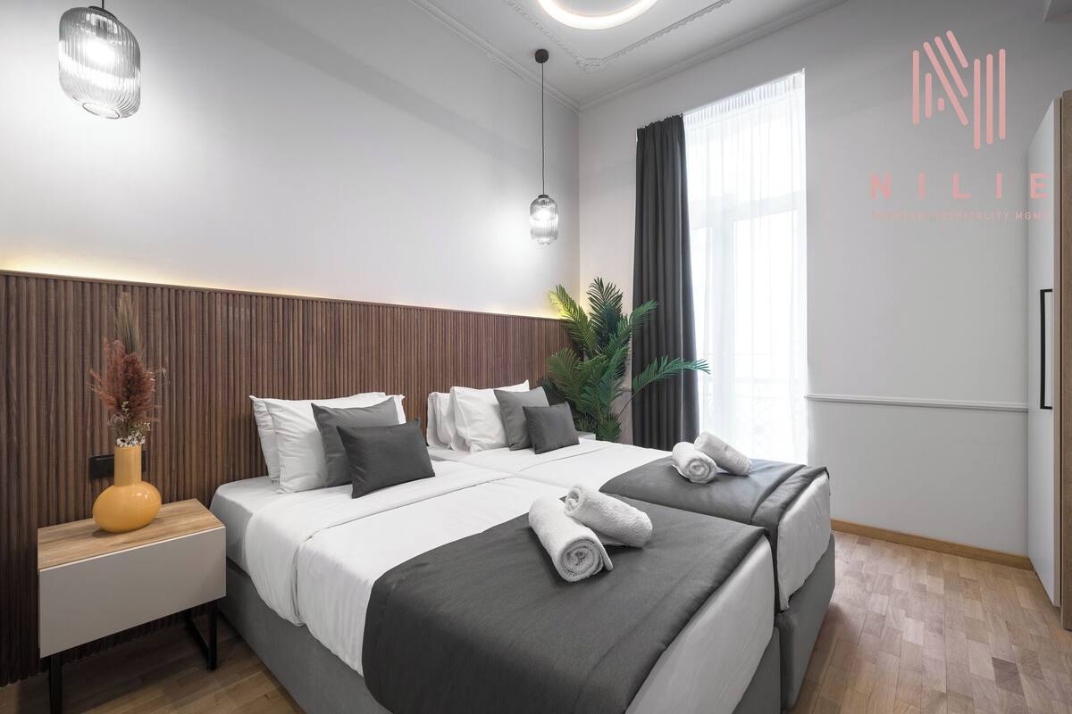 A modern hotel room with a large bed, a bedside table with a vase, and a potted plant.