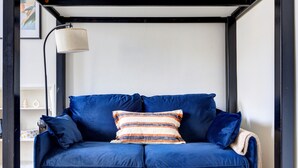 Un sofá azul con almohadones a rayas y una lámpara en una habitación con un marco negro y paredes blancas.
