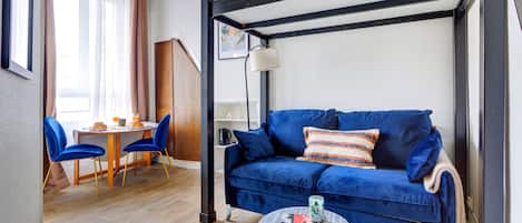 A room with a blue sofa, a small round table, and a dining area with chairs and a table.