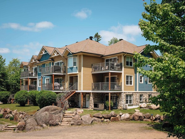 A multi-story building with balconies, a stone foundation, and a staircase leading to the entrance.
