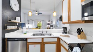 Een moderne keuken met een vaatwasser, fornuis, magnetron, en een klok aan de muur.