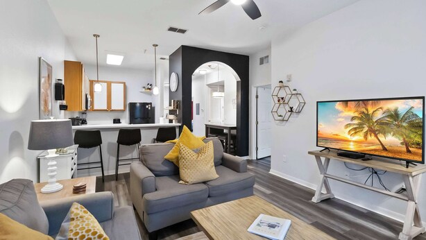 Een moderne woonkamer met een bank, salontafel en televisie. Er is een keukenhoek met een eettafel en stoelen.
