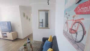 Un salon avec un canapé, une télévision, un miroir et une affiche représentant un vélo.