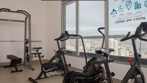 Une salle de sport équipée de matériel d’exercice, d’un banc et d’une fenêtre donnant sur la ville.