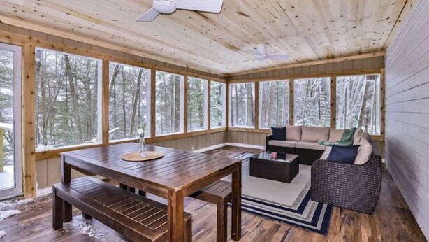 L’intérieur d’un chalet en bois comprend une table à manger, des bancs, un canapé et un ventilateur de plafond.