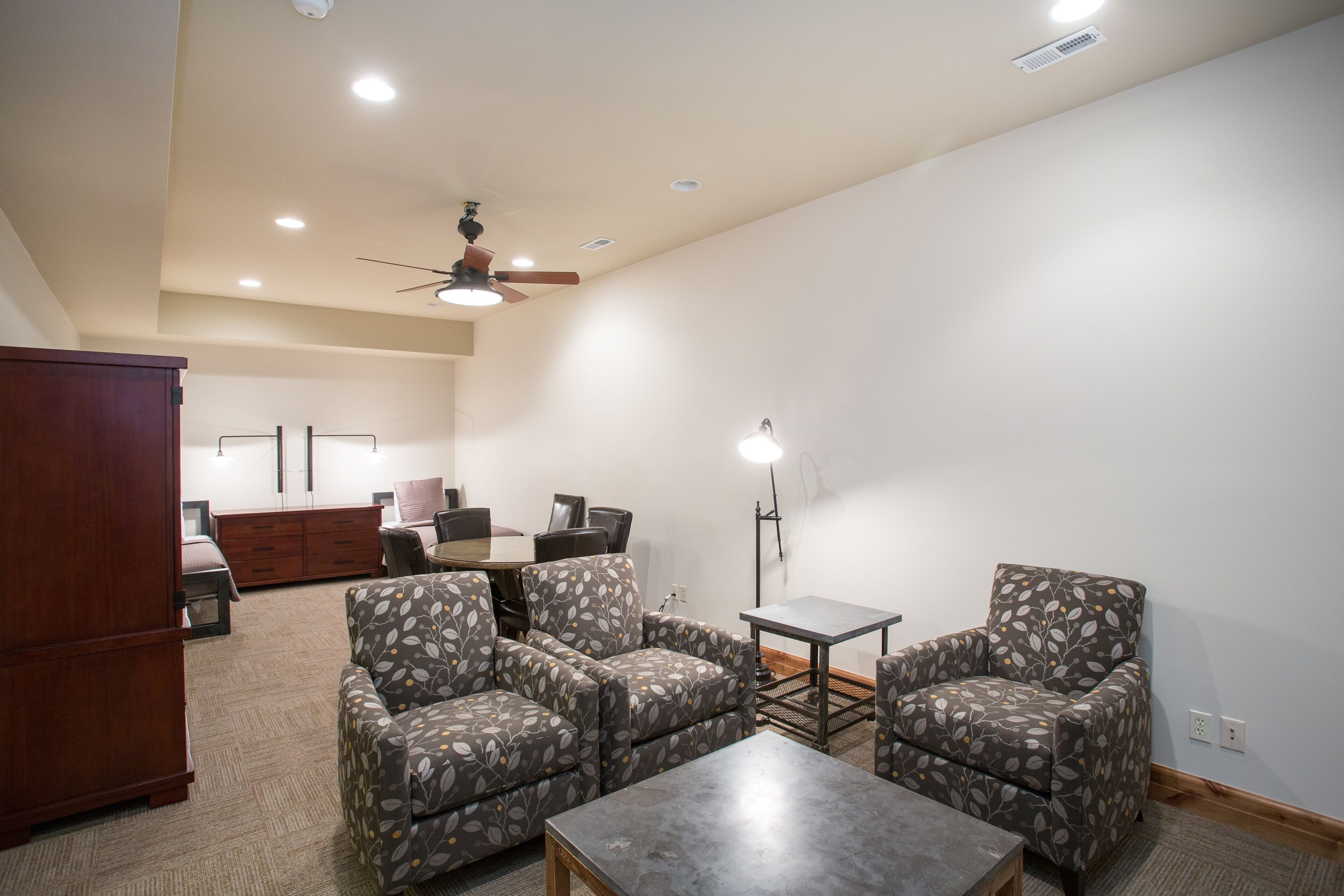 A spacious living room with a ceiling fan, a dining table with chairs, and a large cabinet.