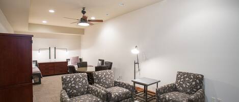 A spacious living room with a ceiling fan, a dining table with chairs, and a large cabinet.