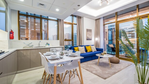 Eine moderne Wohnung mit Essbereich, einem blauen Sofa und großen Fenstern mit Blick auf die Stadt.