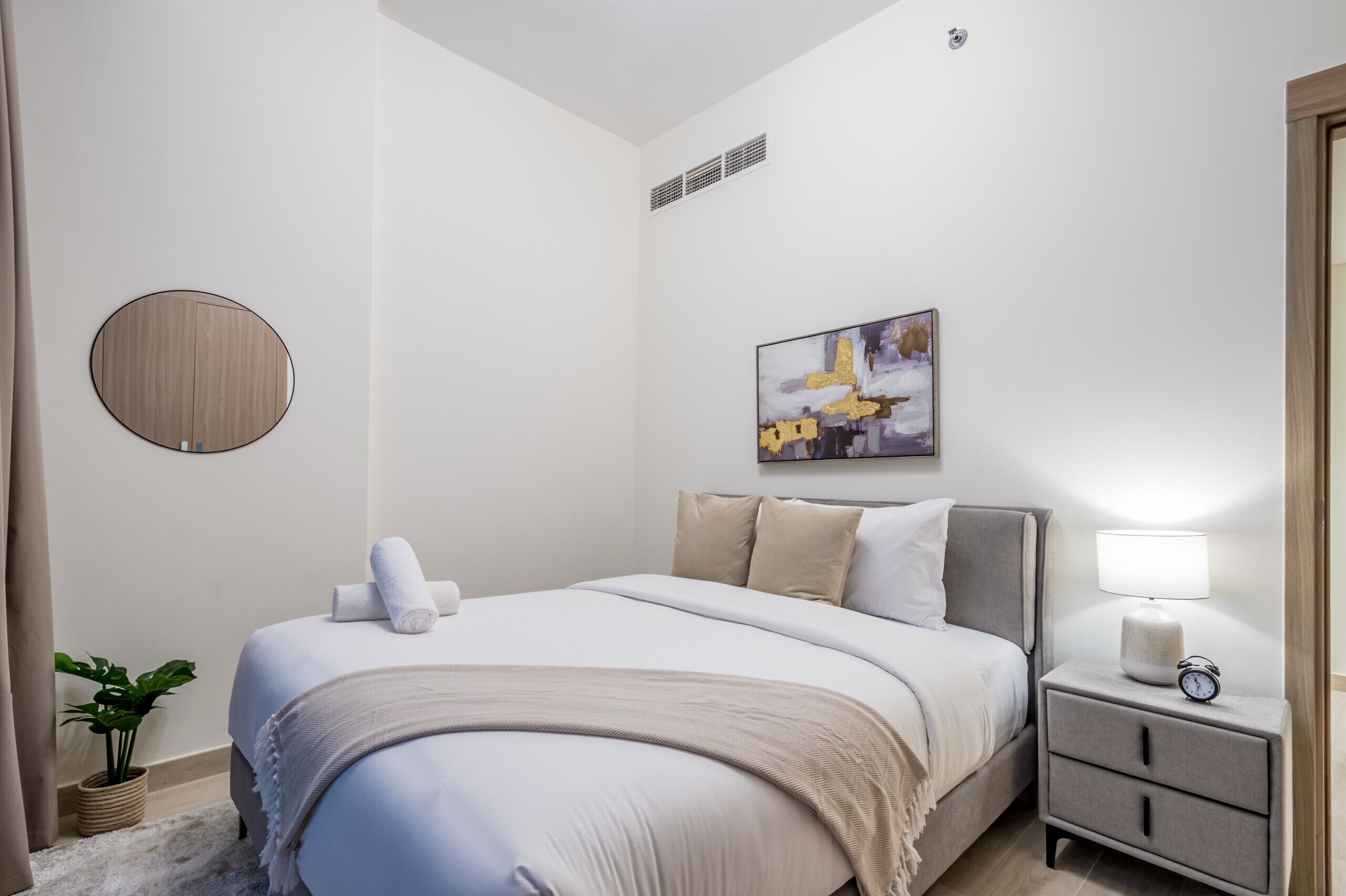 Un dormitorio ordenado con cama, mesita de noche, lámpara y un cuadro colgado en la pared.