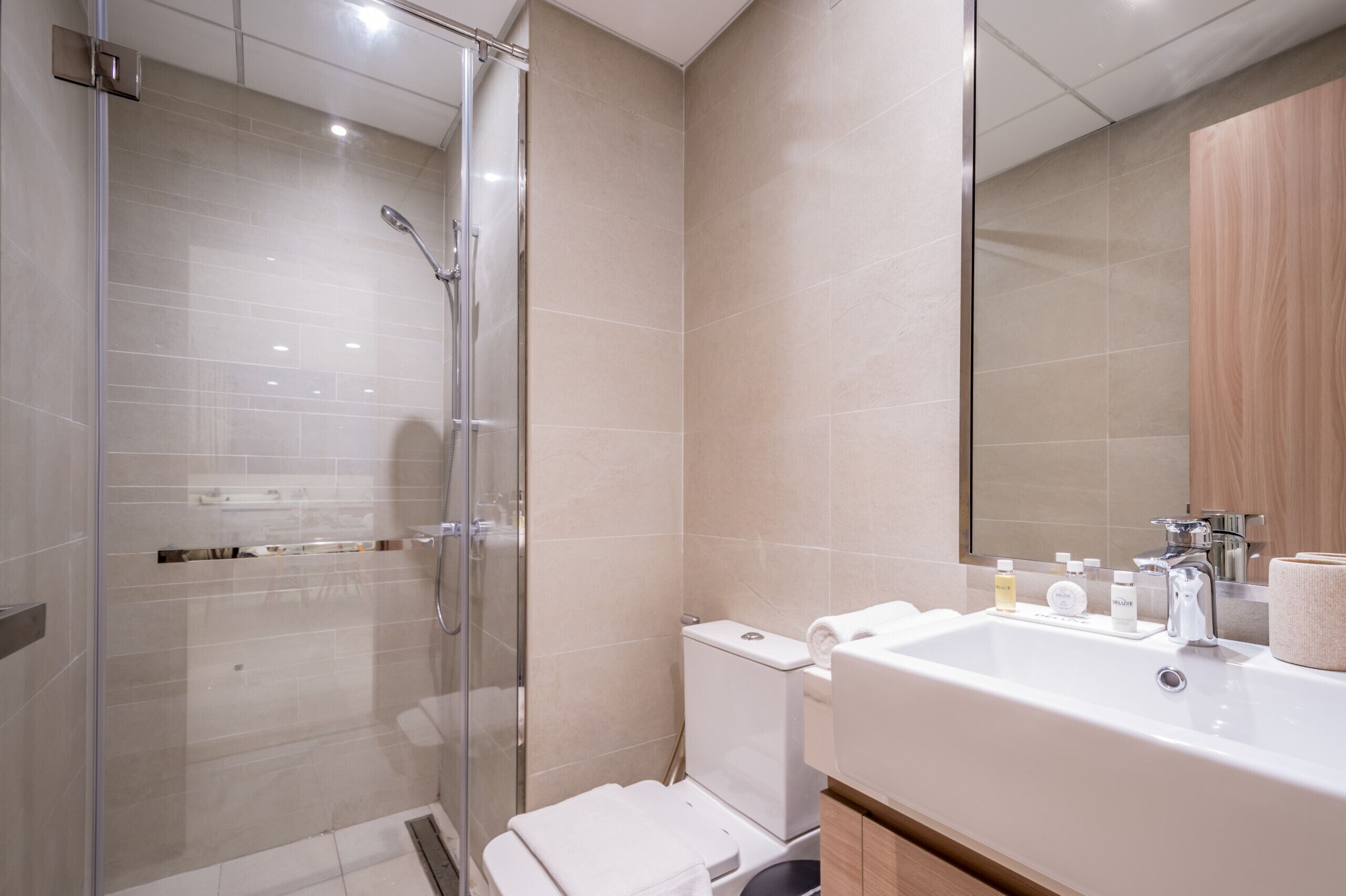 A modern bathroom with a glass-enclosed shower, a white sink with toiletries, and a wooden cabinet.