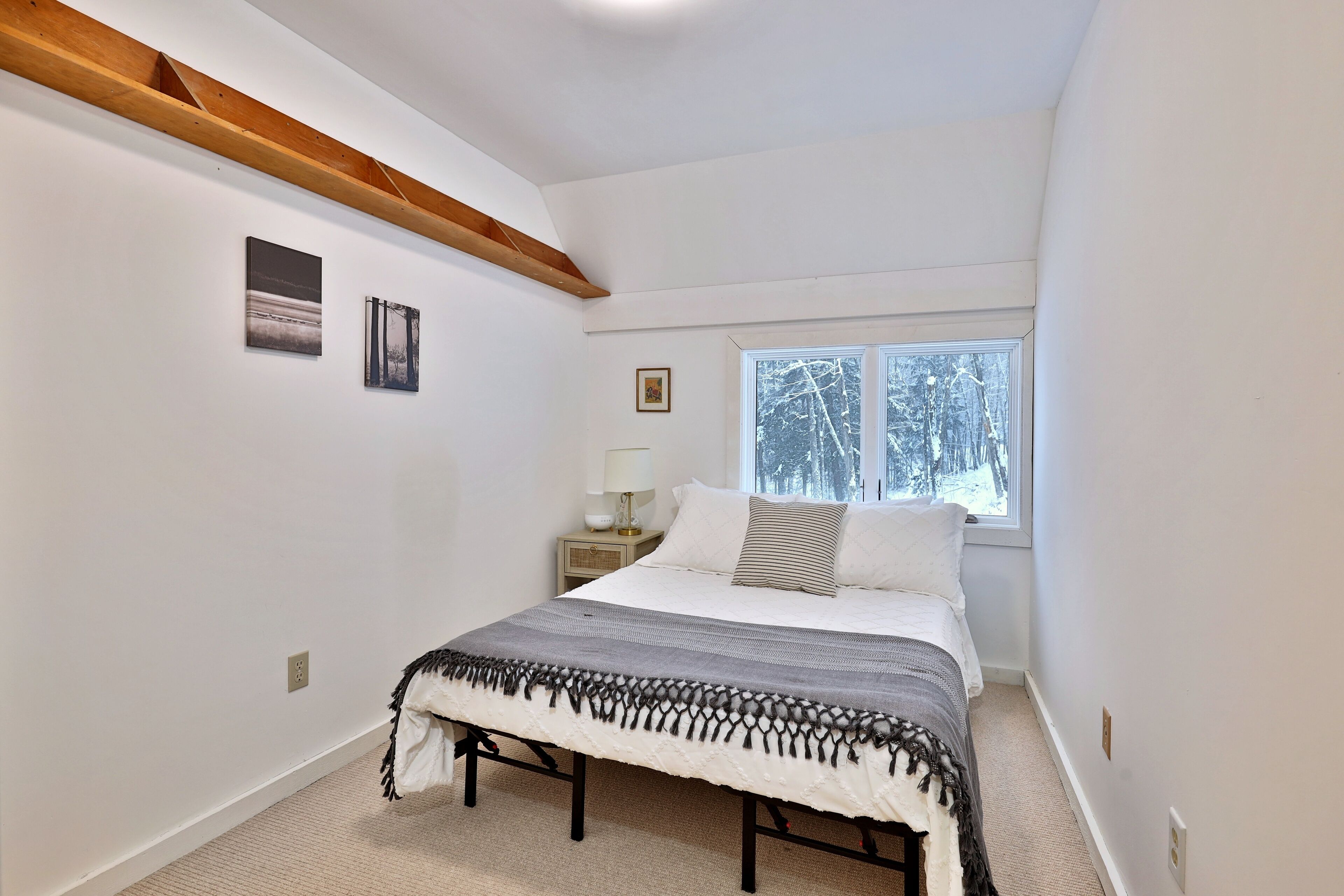 A bedroom with a bed, a window, a nightstand, and wall-mounted pictures.
