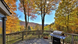 A deck with a grill, overlooking a forest with autumn foliage. - Mountainview Escape 4 Bedroom Home (Killington)