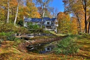 A house with a stone bridge over a stream, surrounded by autumn foliage. - Mountainview Escape 4 Bedroom Home (Killington)