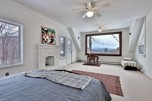 A bedroom with a large bed, a fireplace, a view of the outdoors, and a ceiling fan. - Mountainview Escape 4 Bedroom Home (Killington)