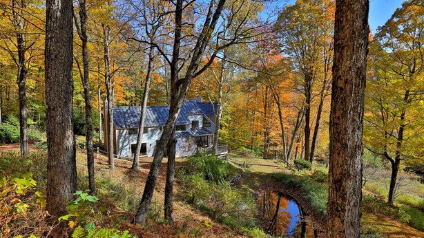 A rustic cabin surrounded by autumn foliage, a small stream, and a wooden deck. - Mountainview Escape 4 Bedroom Home (Killington)