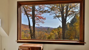 A room with a large window overlooking a forested area with autumn foliage. - Mountainview Escape 4 Bedroom Home (Killington)