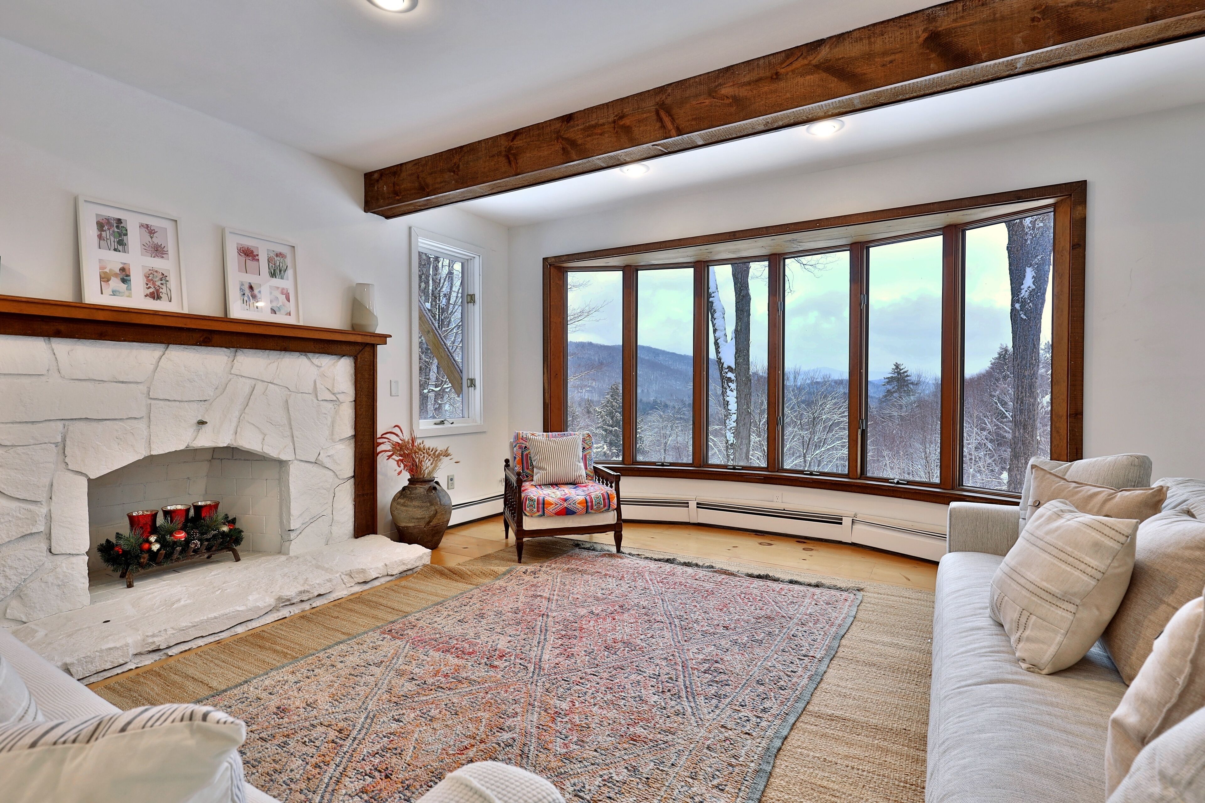 A cozy living room with a stone fireplace, a large window with a view of trees, and a comfortable seating area.